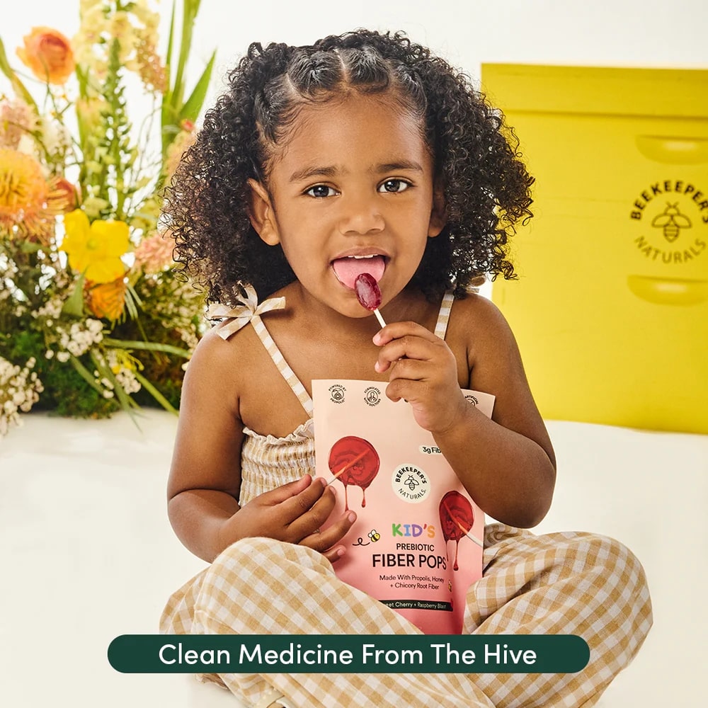 Child holding a package of 'Beekeeper Naturals' fiber pops with flowers and a yellow container in the background.