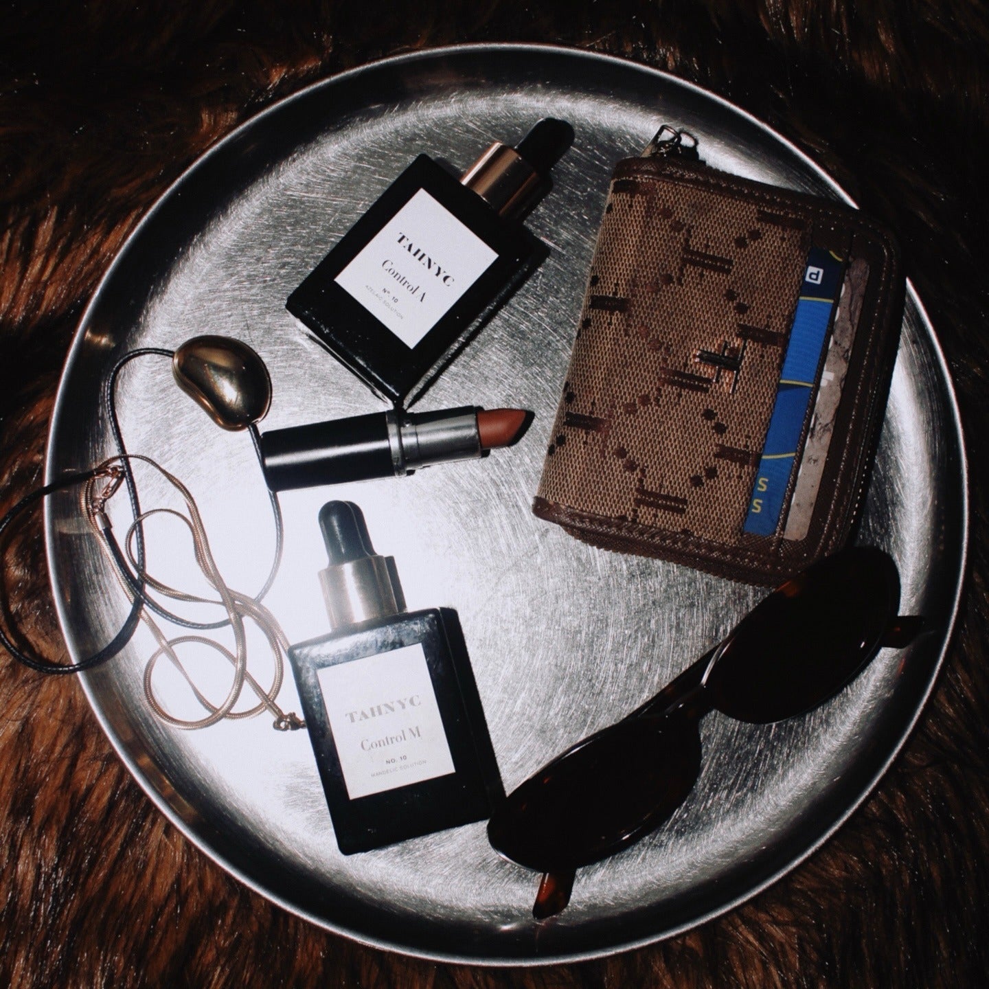 Tray with lipsticks, perfumes, wallet, and sunglasses on a fur surface