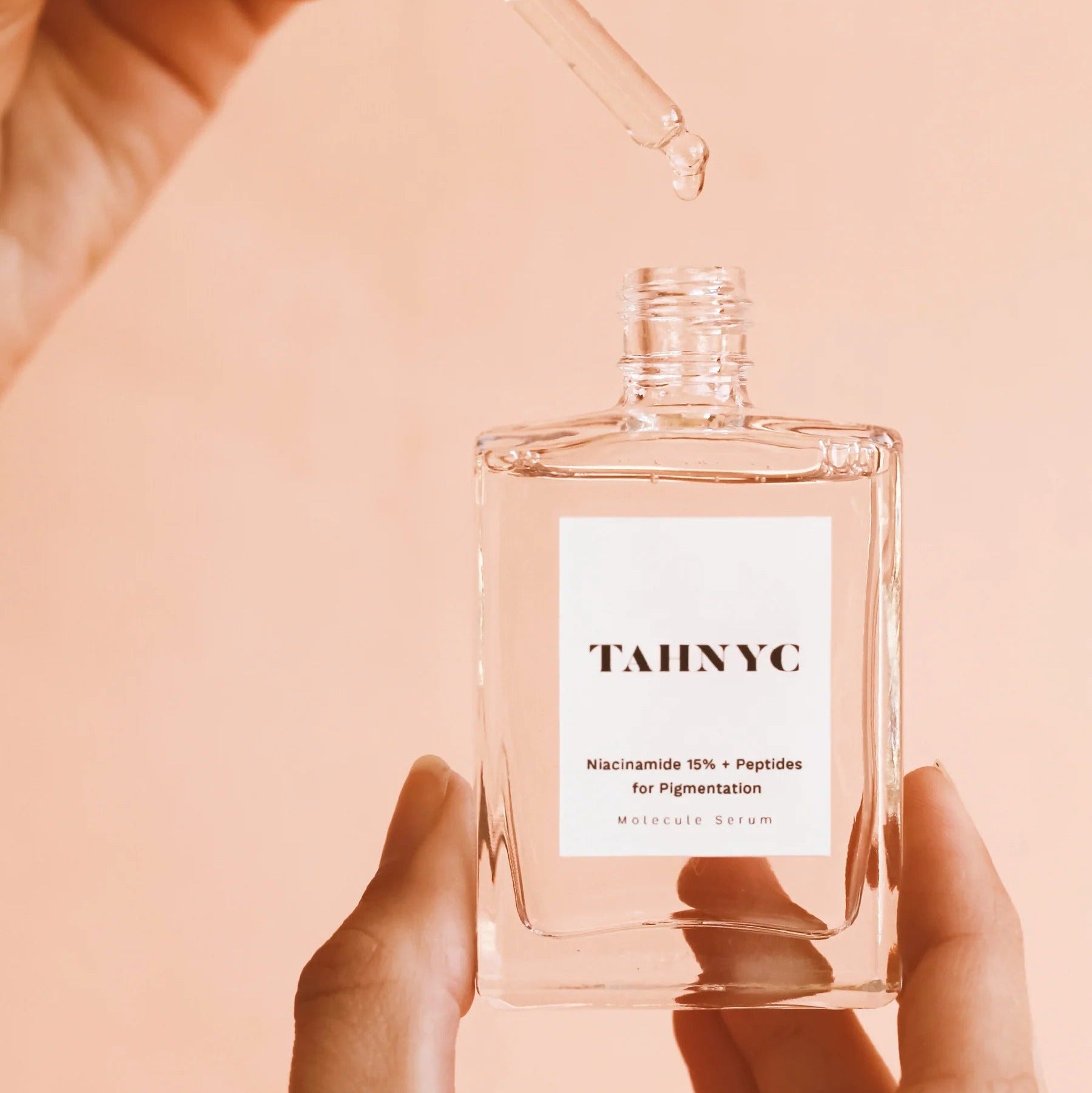 Hands holding TAHNYC Niacinamide 15% + Peptides Serum bottle during application – The Pharmacy Lab
