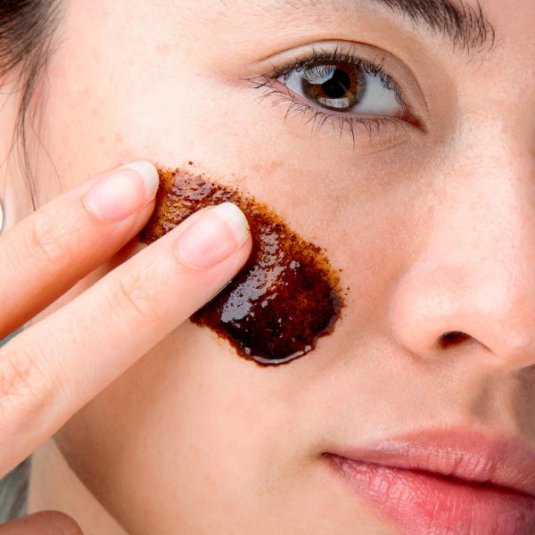 Close-up of a woman applying a brown paste to her face.