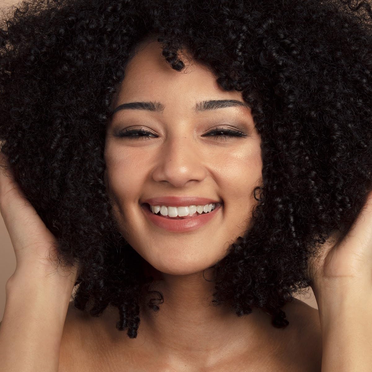 Woman with curly hair smiling against a neutral background