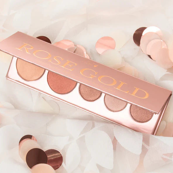 Rose gold makeup palette with lip glosses on a soft white background
