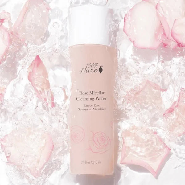 Bottle of 100% Pure Rose Micellar Cleansing Water surrounded by pink rose petals on a white background