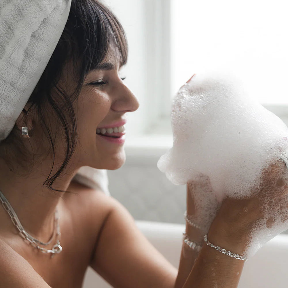 Woman with a towel on her head holding a bubble bath sponge with bubbles.