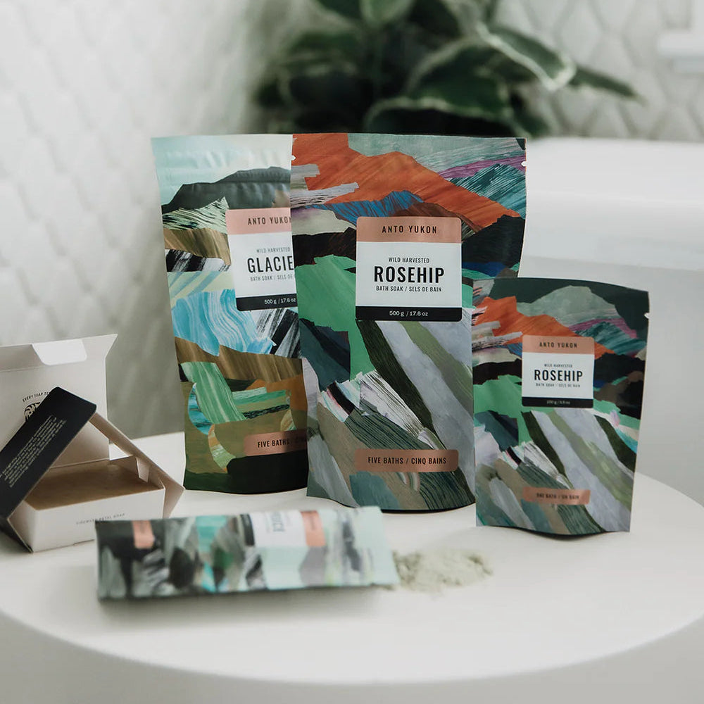 Tea packages with colorful designs on a white surface with a plant in the background