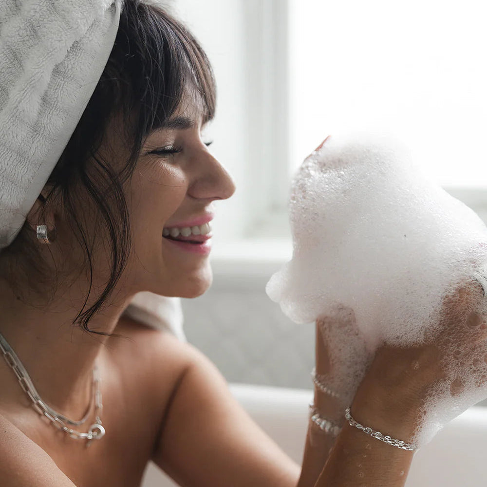 Woman with a towel on her head holding a bubble bath sponge with bubbles.