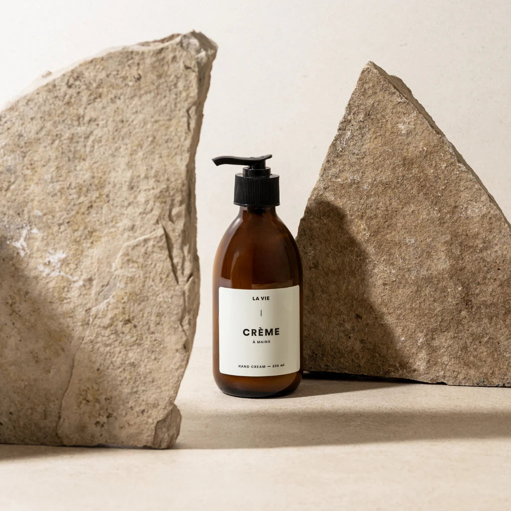 Cosmetic bottle labeled 'La Vie Crème' between two large stones on a neutral background