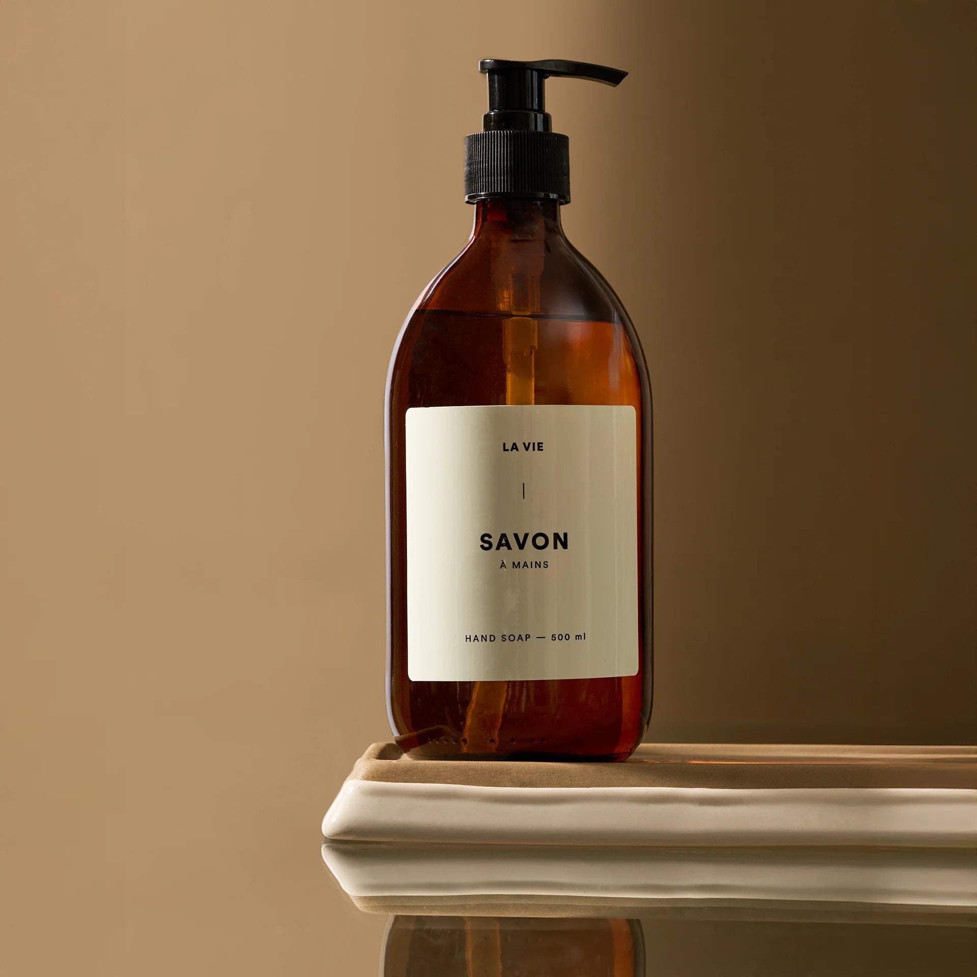 Brown soap bottle with pump and 'La Vie' label on a beige surface and background