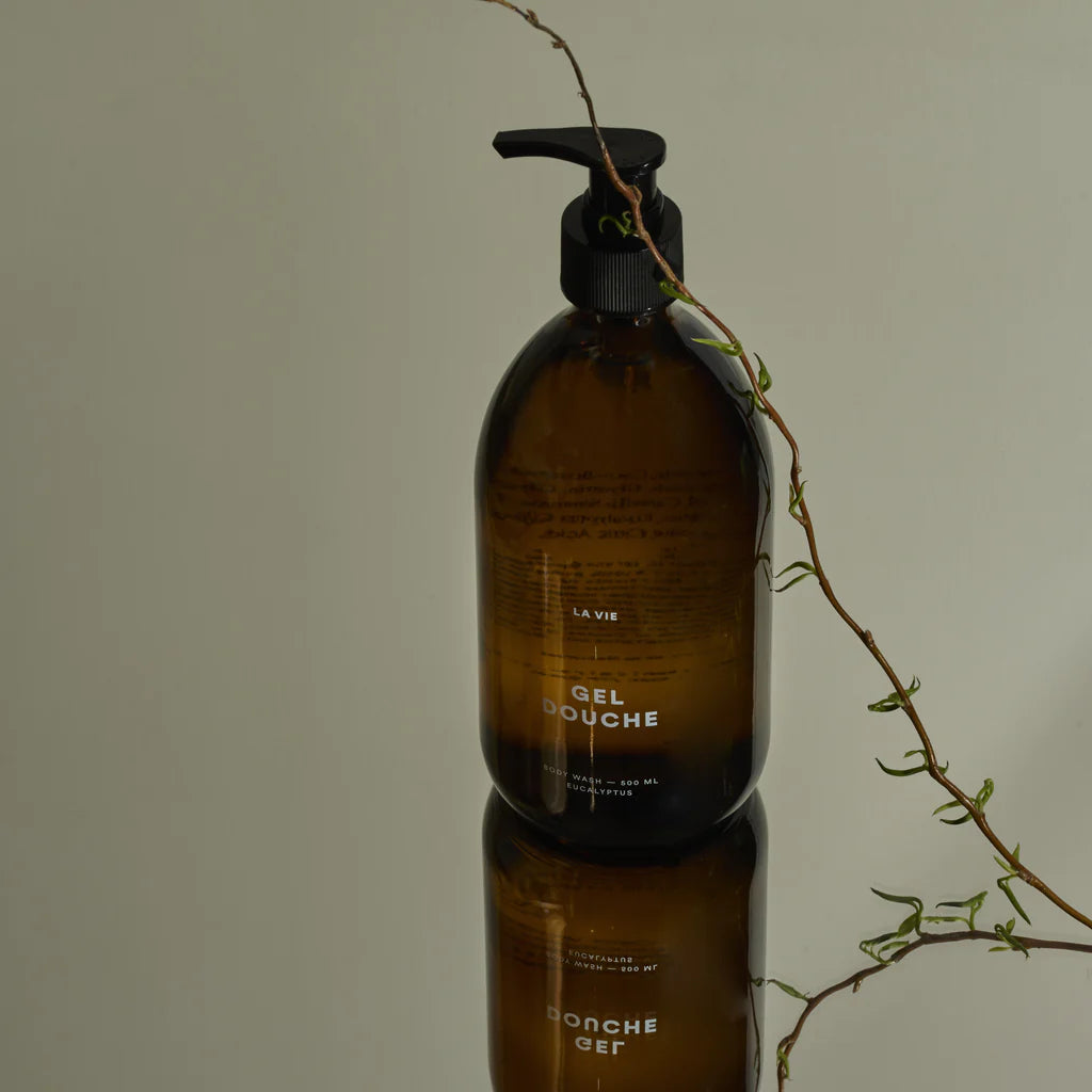 Brown bottle with pump dispenser on a reflective surface, with a branch in the background.