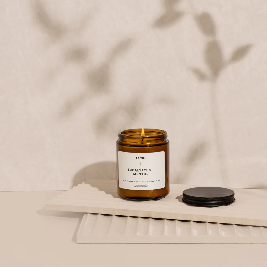 Candle in a amber jar with a white label on a beige surface with plant shadows