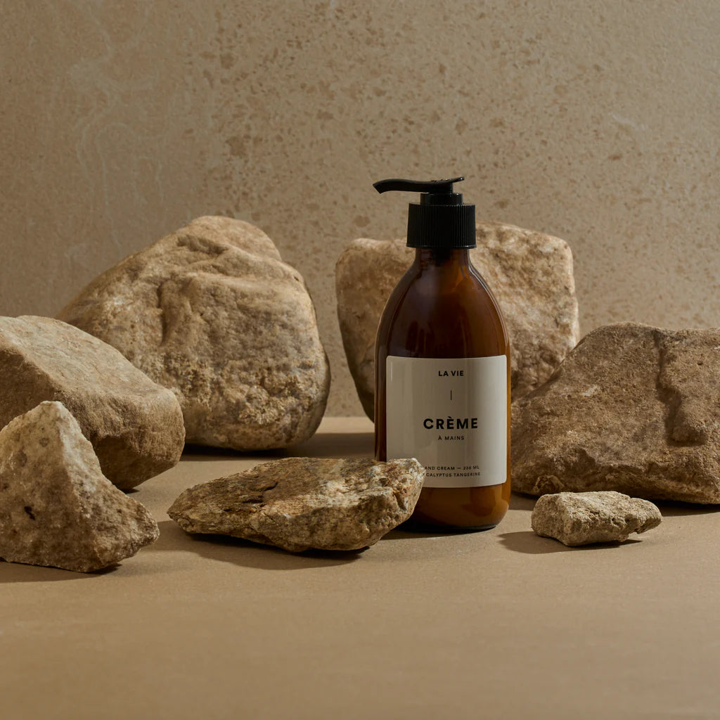 Bottle labeled 'La Vie Crème' surrounded by rocks on a beige background