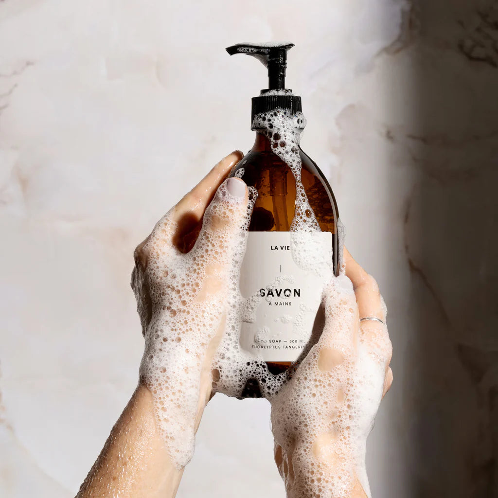 Hand holding a bottle of soap labeled 'La Vie' with a marble background