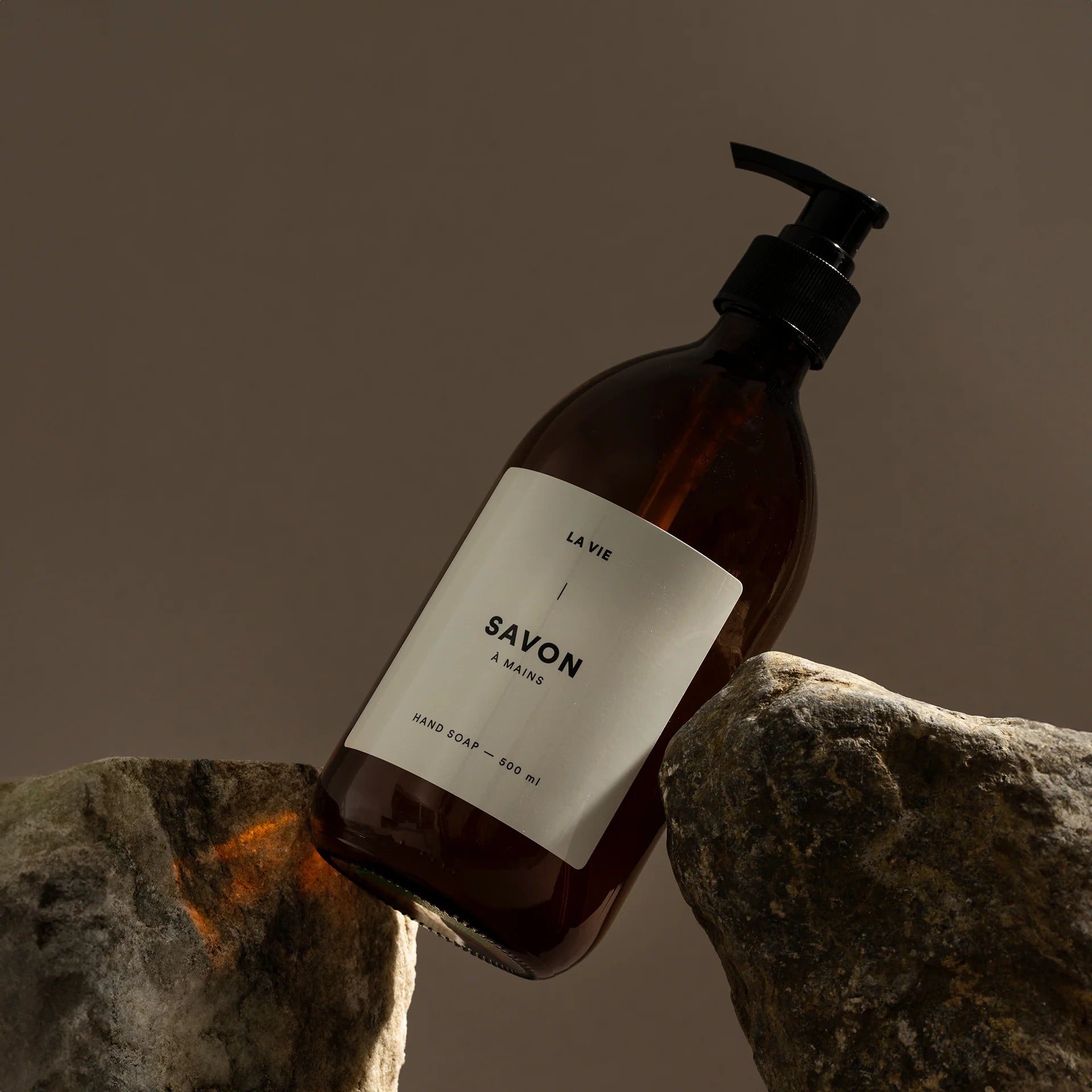 Brown soap bottle with pump on a stone surface against a brown background
