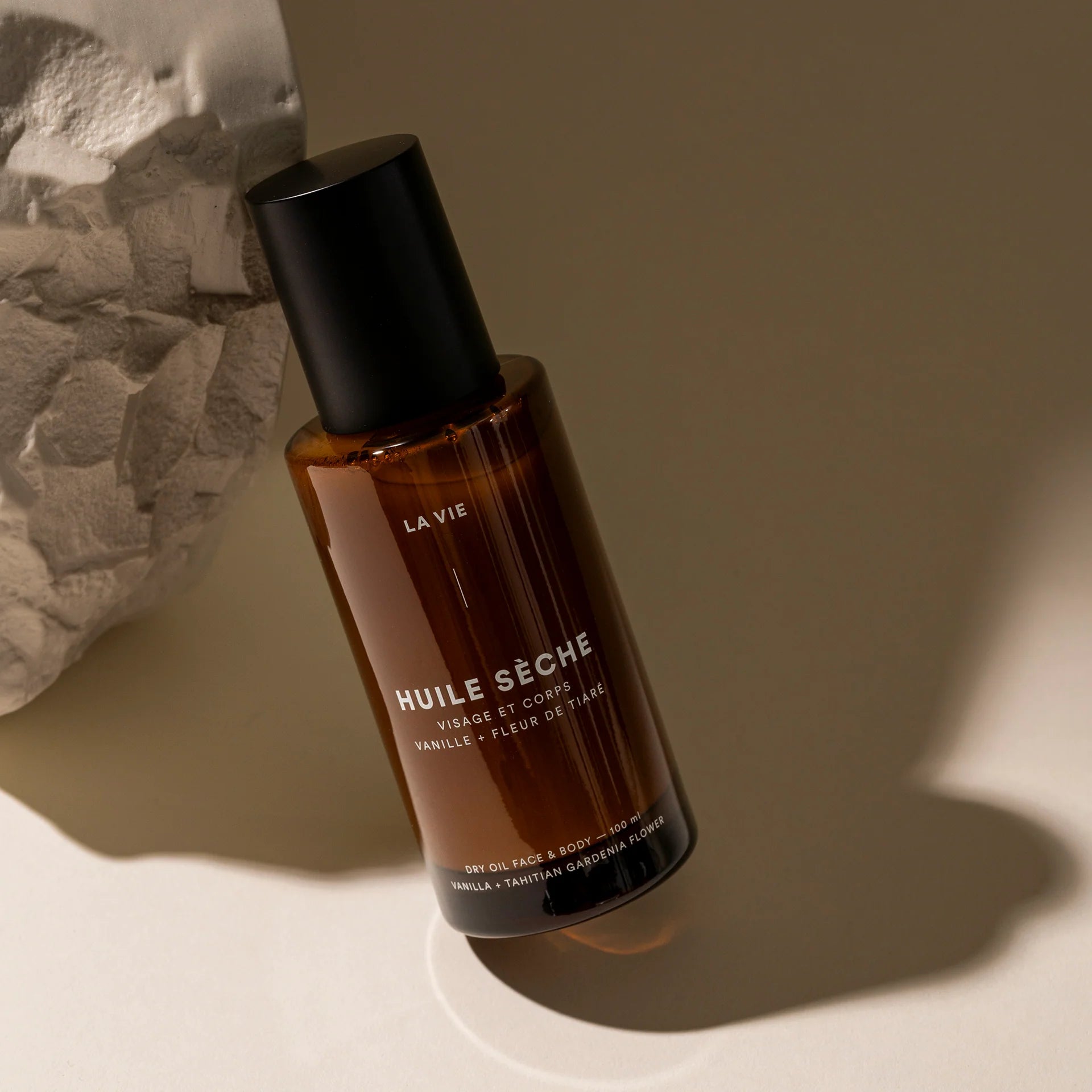 Brown bottle with black cap labeled 'Huile Séche' on a neutral background