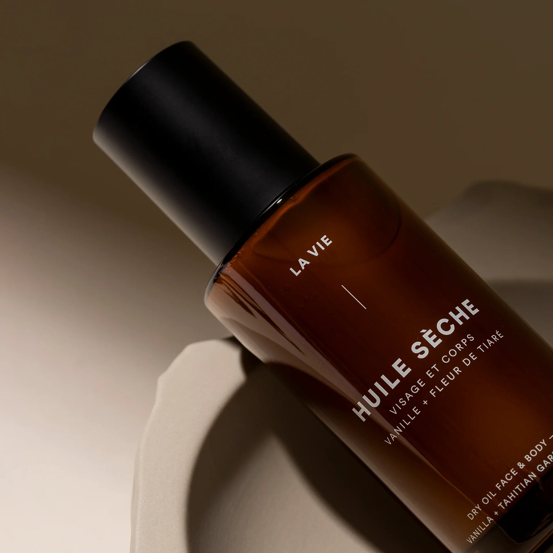Brown bottle labeled 'HUILE SECHE' with 'LA VIE' on a beige background