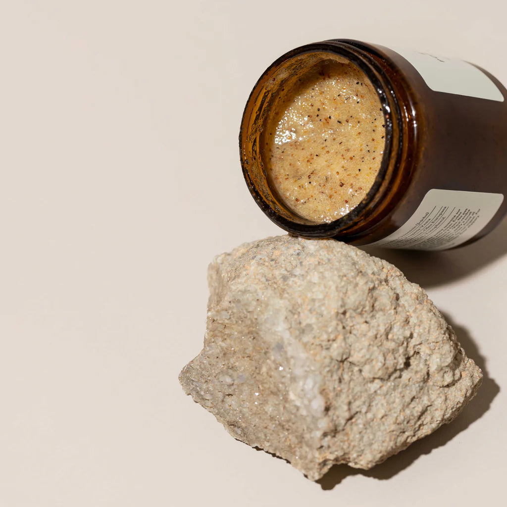 Open jar of a beige substance next to a rock on a beige background