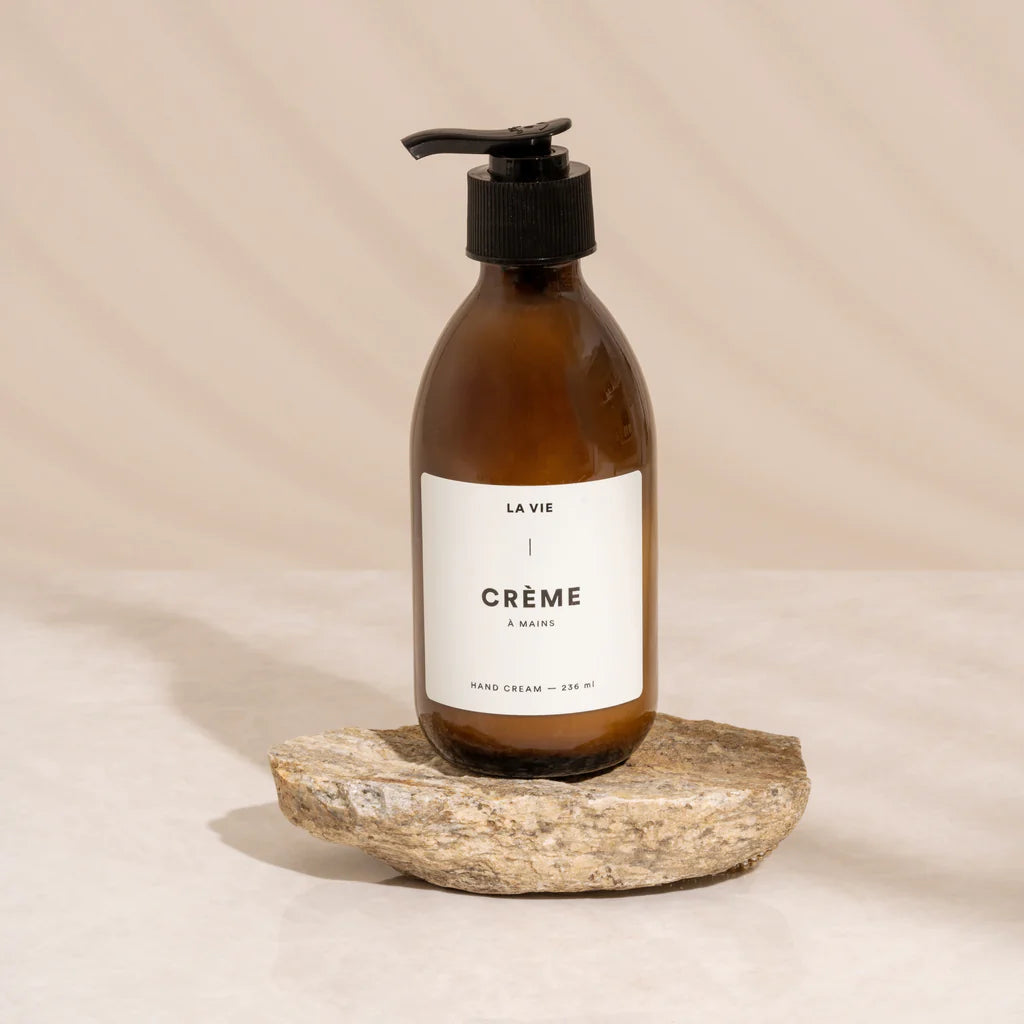 Hand cream bottle labeled 'La Vie Crème' on a natural stone surface with a beige background