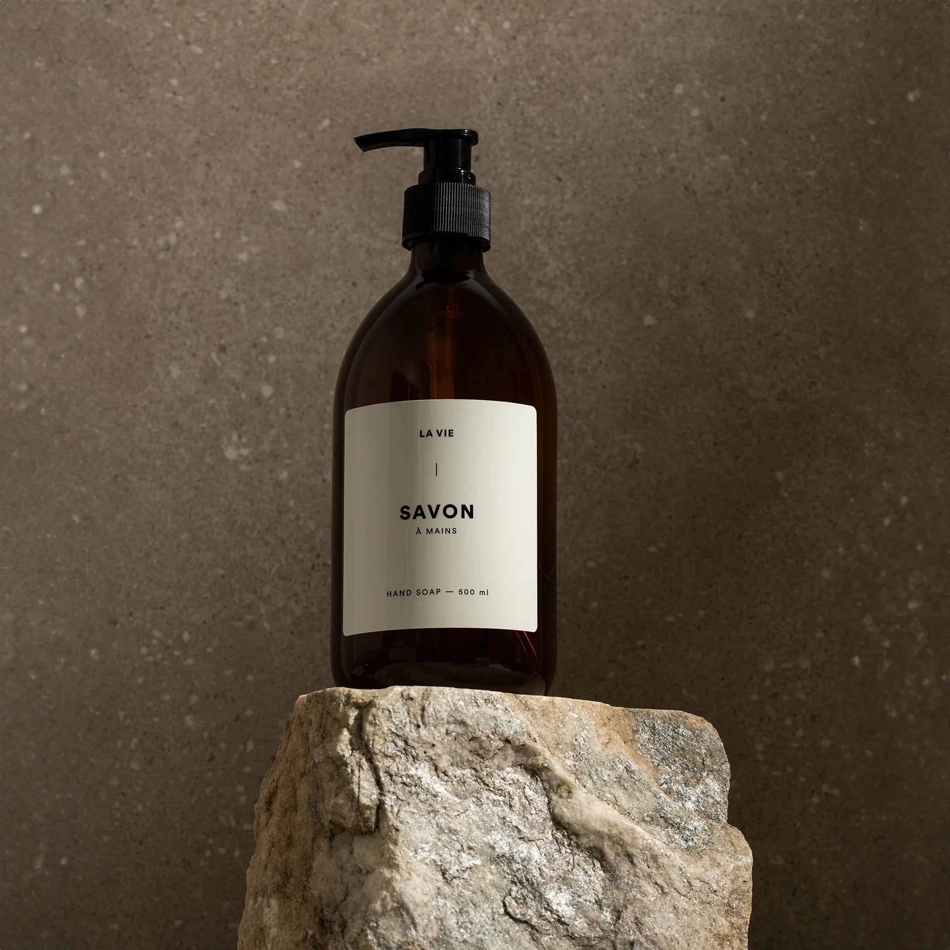 Brown soap bottle with pump on a stone surface against a brown background