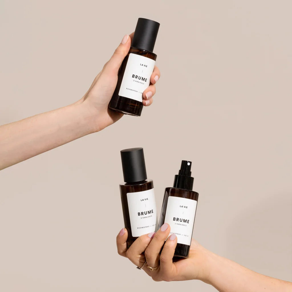 Three 'BRUME' bottles held by hands against a beige background