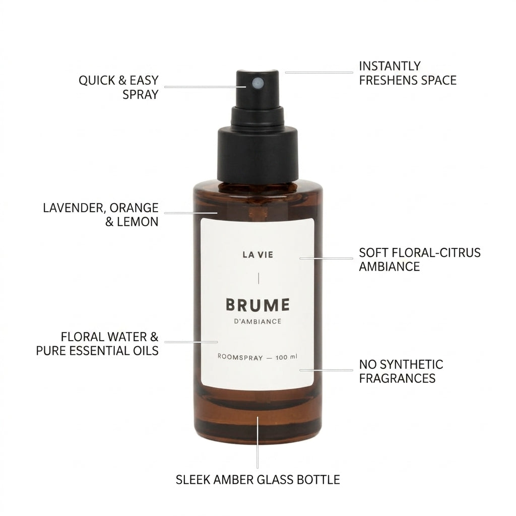 A 100 ml room spray bottle from Brume d'Ambiance by La Vie, in a sleek amber glass bottle with a black spray nozzle and a white label. The image features multiple text callouts with lines pointing to the product, explaining its scent profile (lavender, orange, and lemon), its soft floral-citrus ambiance, and its key features like instant freshening of the space and no synthetic fragrances.