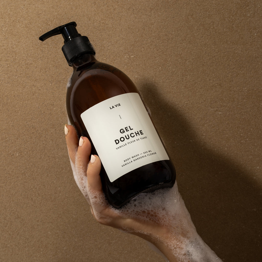Hand holding a bottle of 'La Vie' shower gel against a brown background