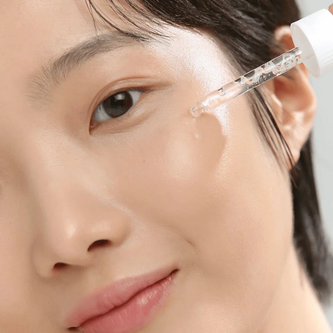 Person applying a skincare product to their face with a dropper.