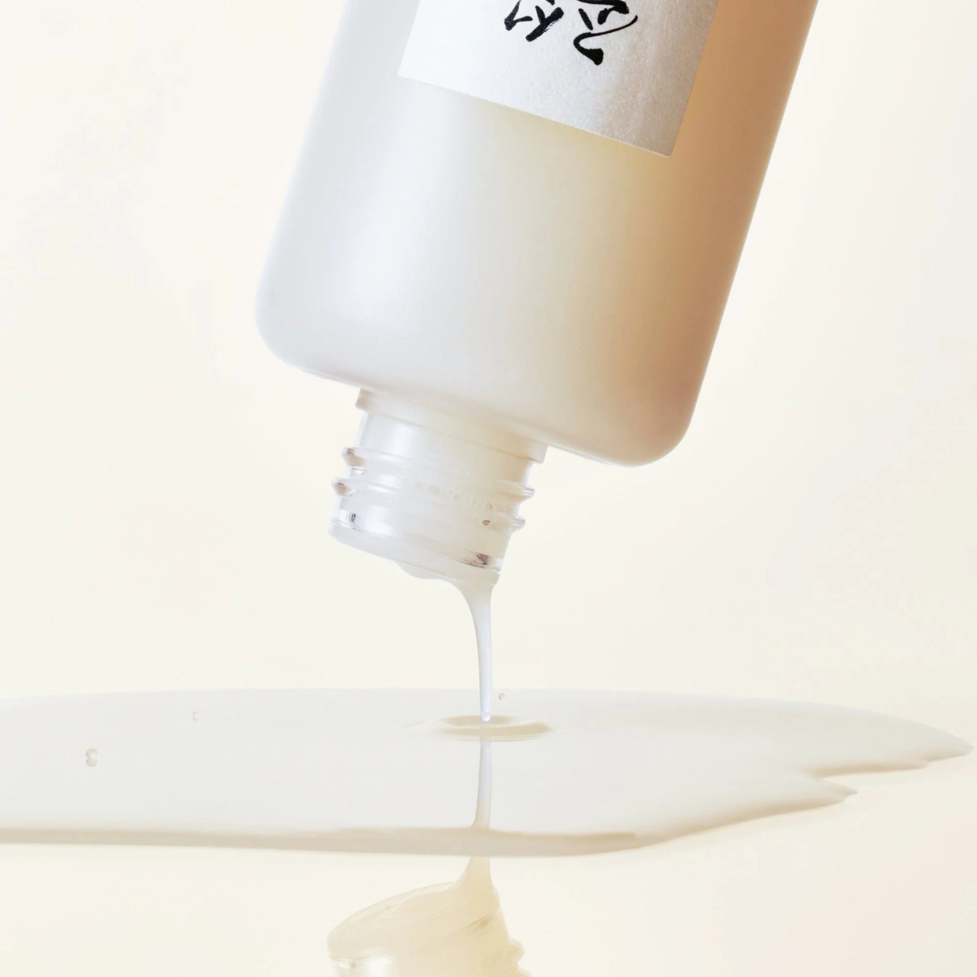 Close-up of a bottle being squeezed, with a focus on the cream-like substance being dispensed.