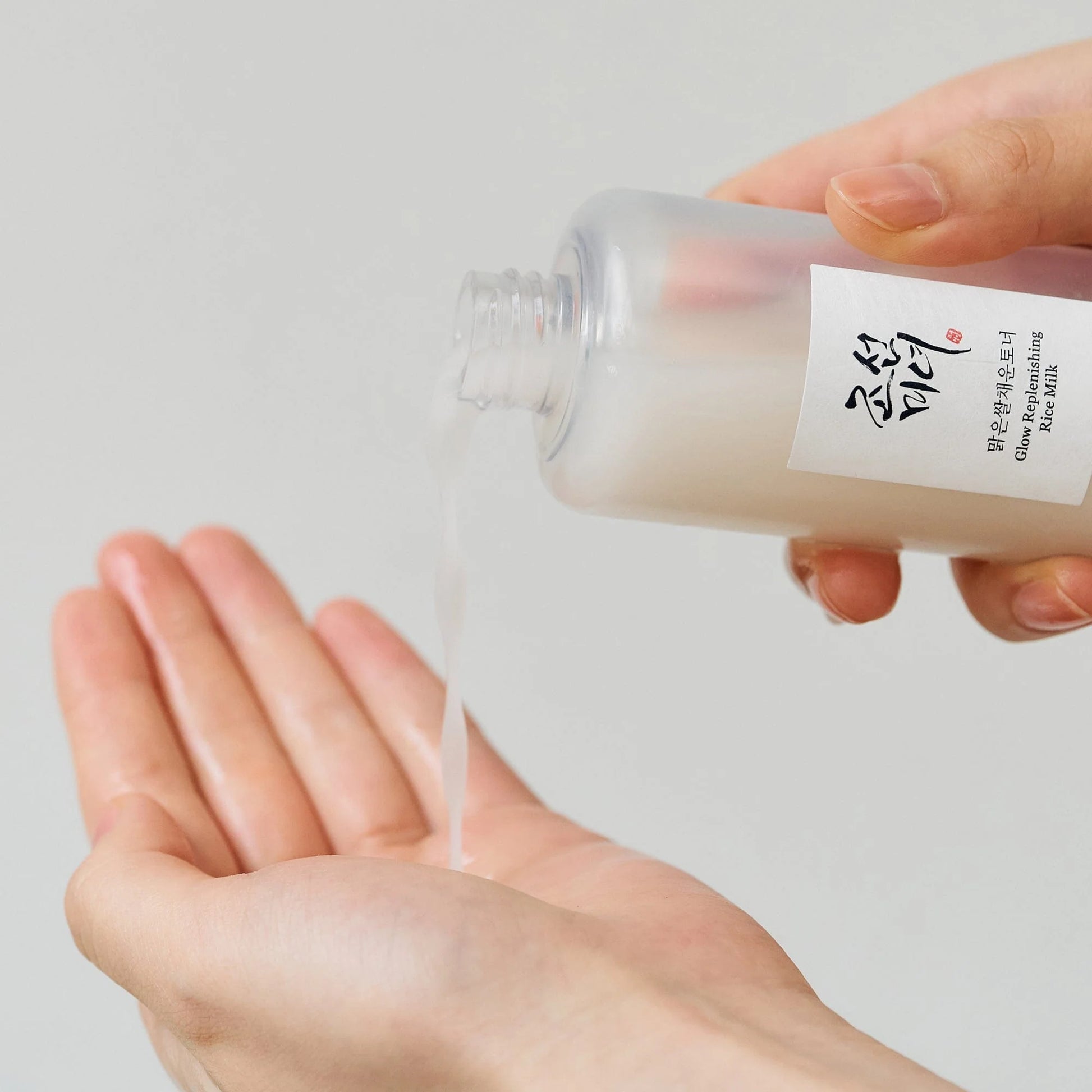 Person holding a small container of rice milk with a white label against a light gray background