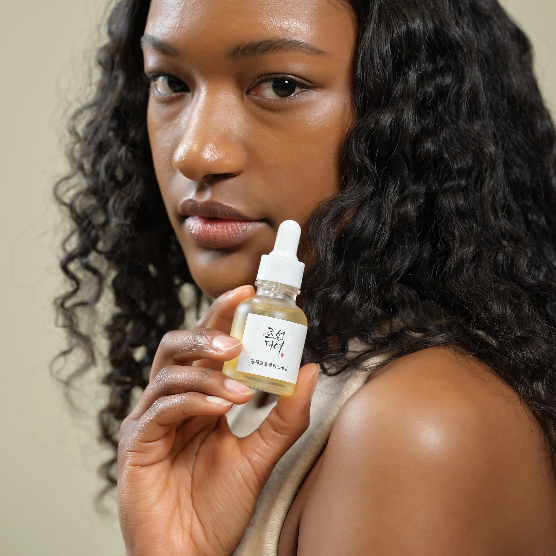 Woman holding a skincare dropper bottle with a neutral background