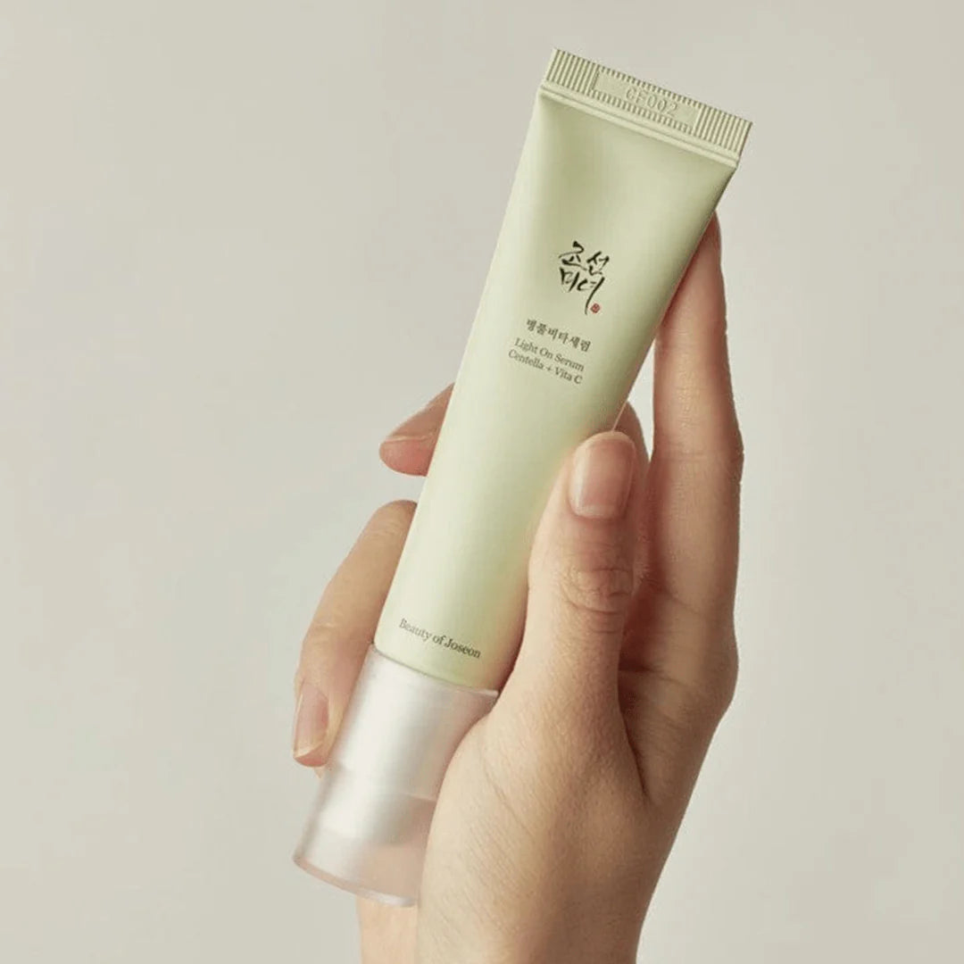 Hand holding a tube of light green cream against a neutral background