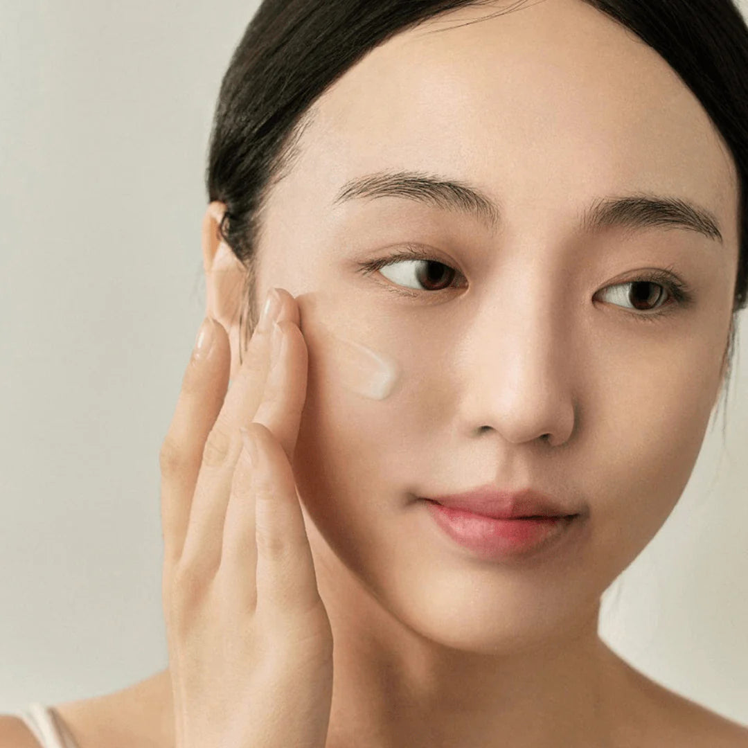 Woman applying cream to her face with a neutral background