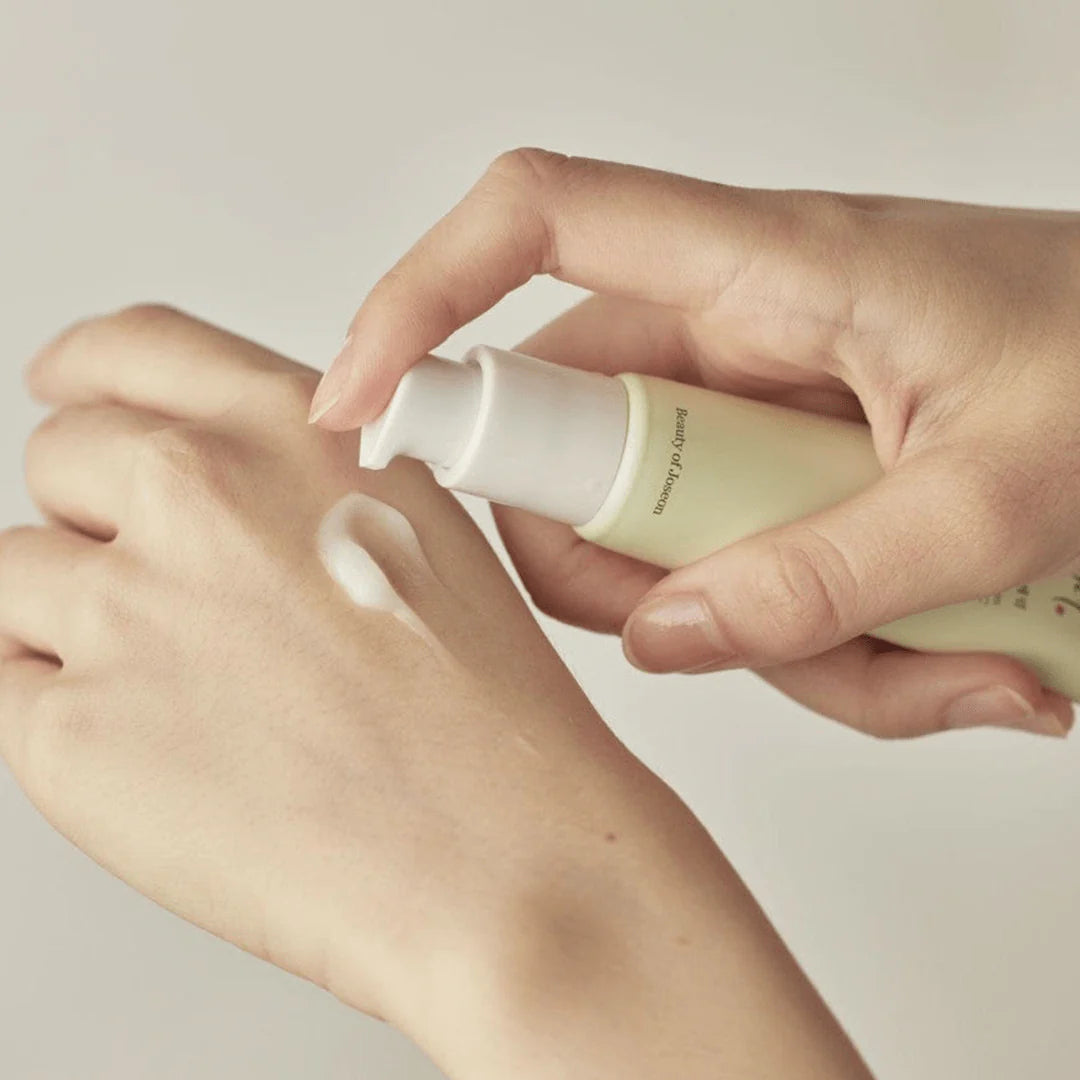 Hand applying a skincare product to another hand on a neutral background