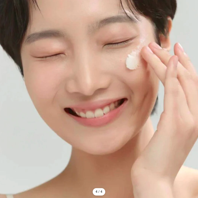Person applying cream to their face with a neutral background