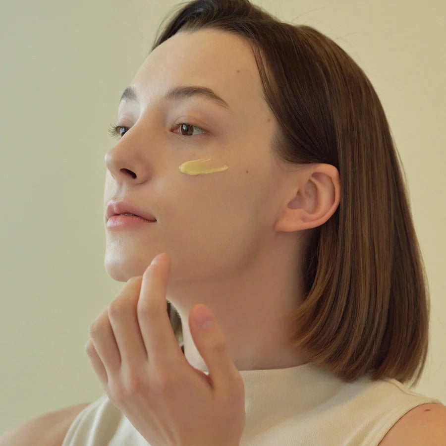 Person applying a yellow cream to their face with a neutral background