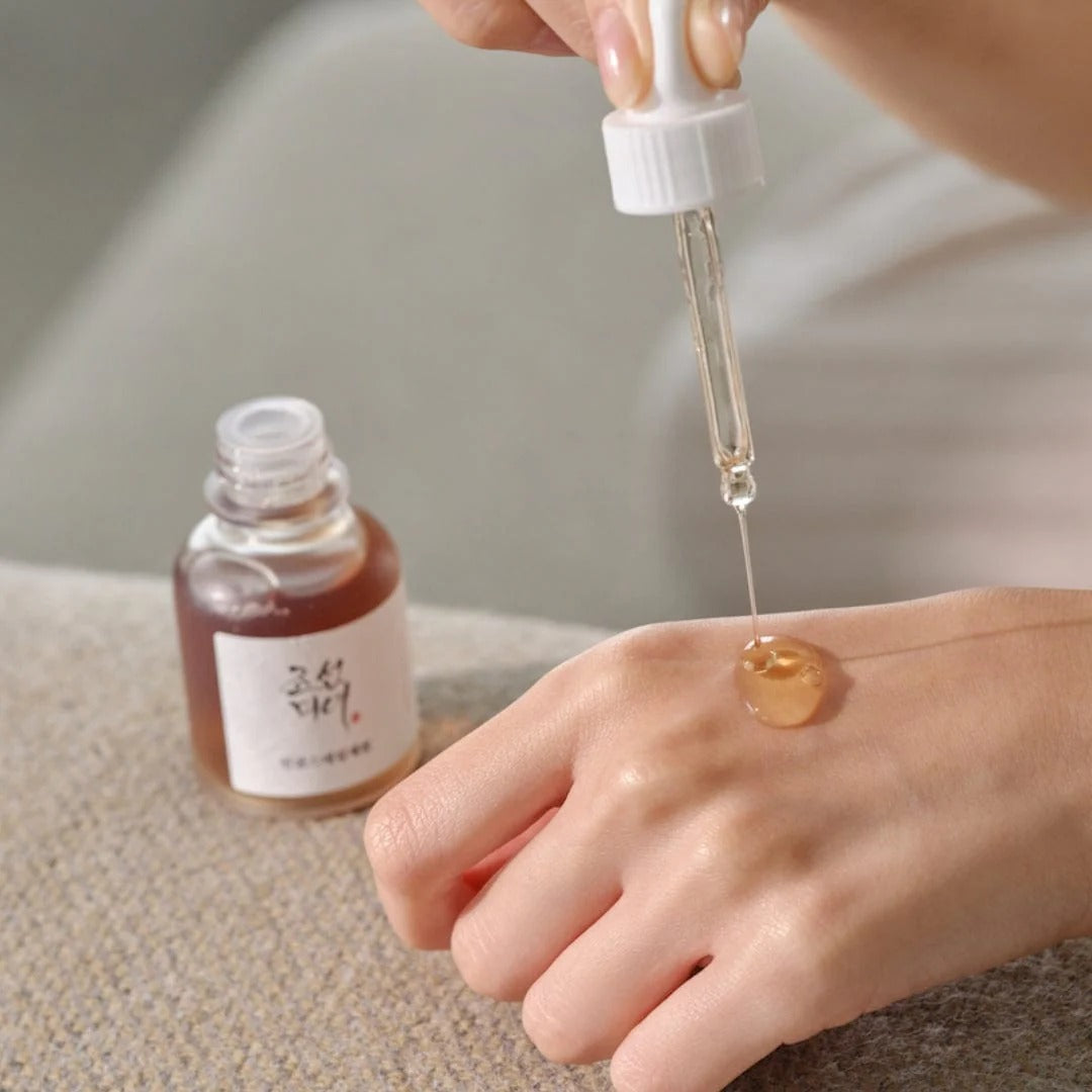 Person applying a dropper of skincare product to their hand with a blurred background