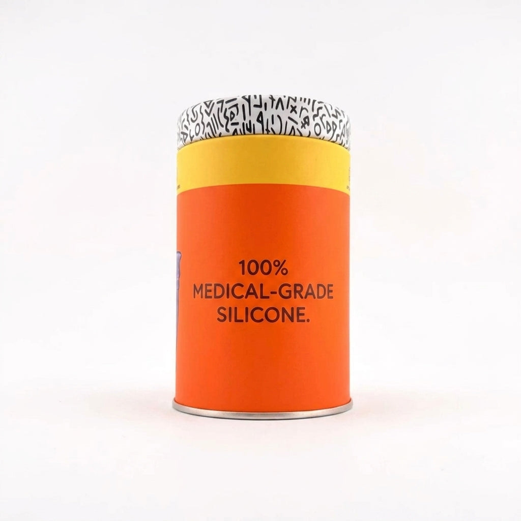 A cylindrical metal tin of medical-grade silicone, featuring a bright orange body with black text, a yellow band, and a black-and-white patterned lid, set against a plain white background.
