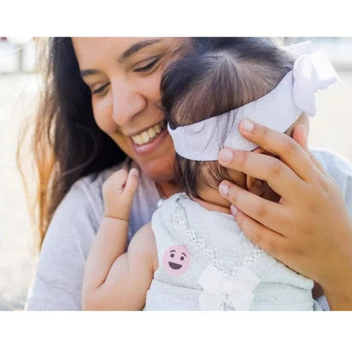 Woman holding a child with a white bow in her hair, both smiling.