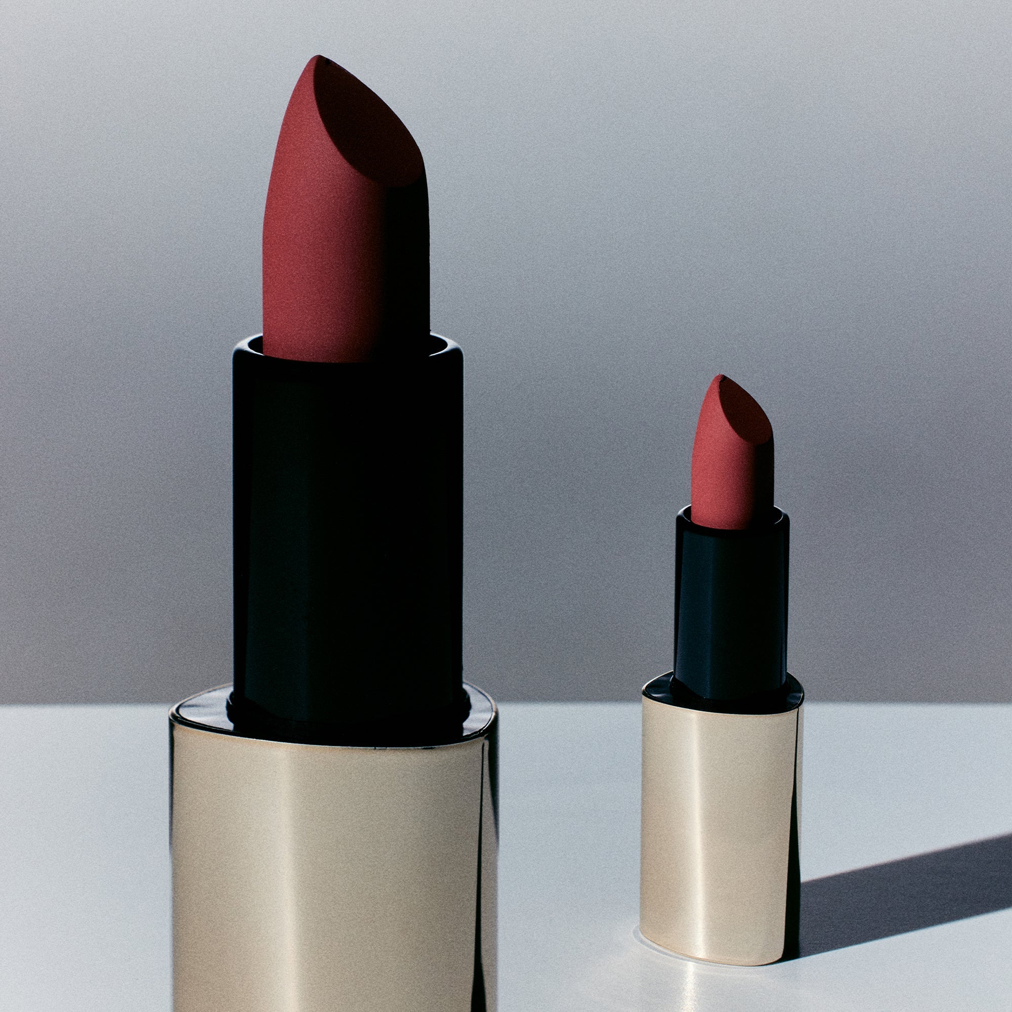 Two lipsticks with black and gold cases on a light gray background