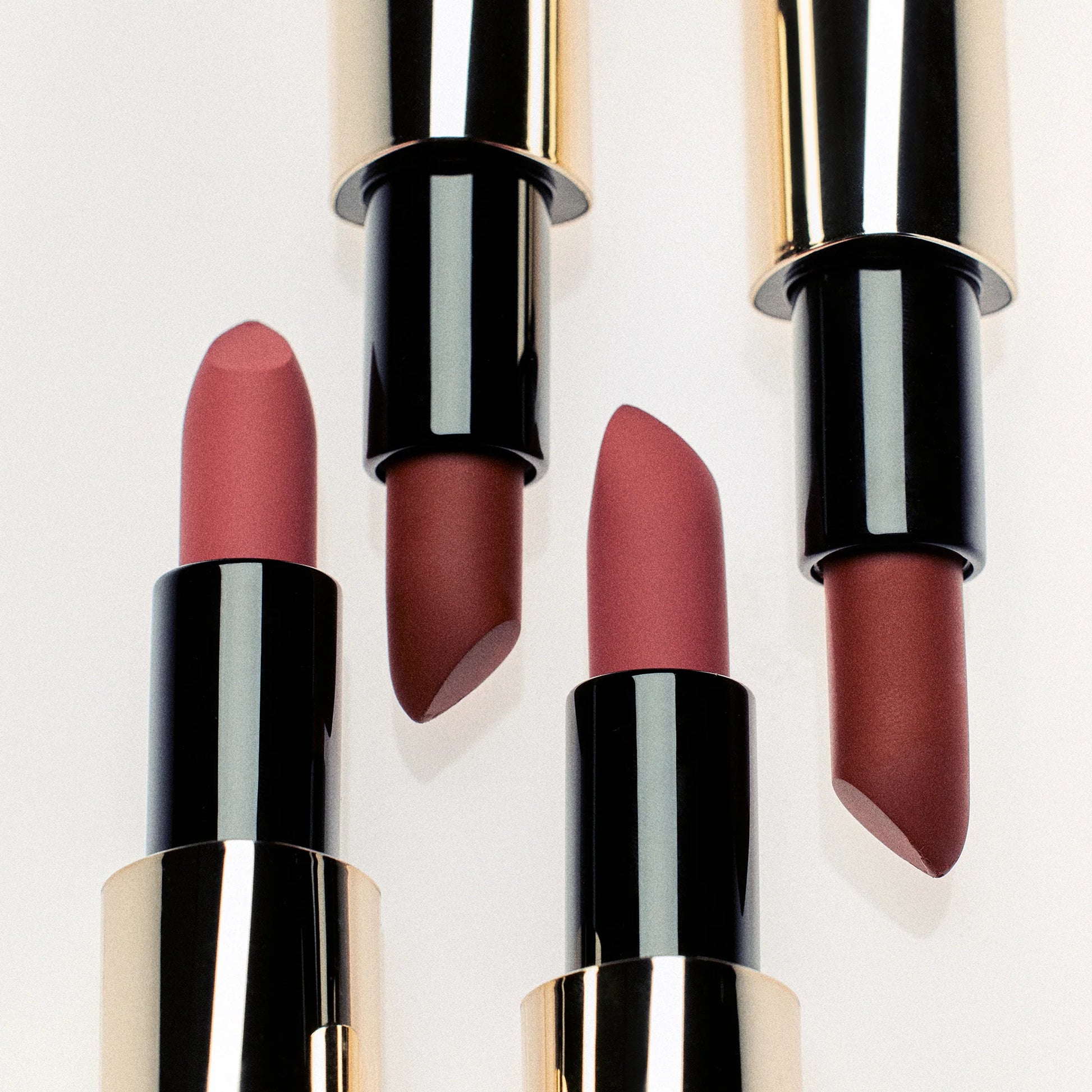 Set of four lipsticks with black and gold cases on a light background