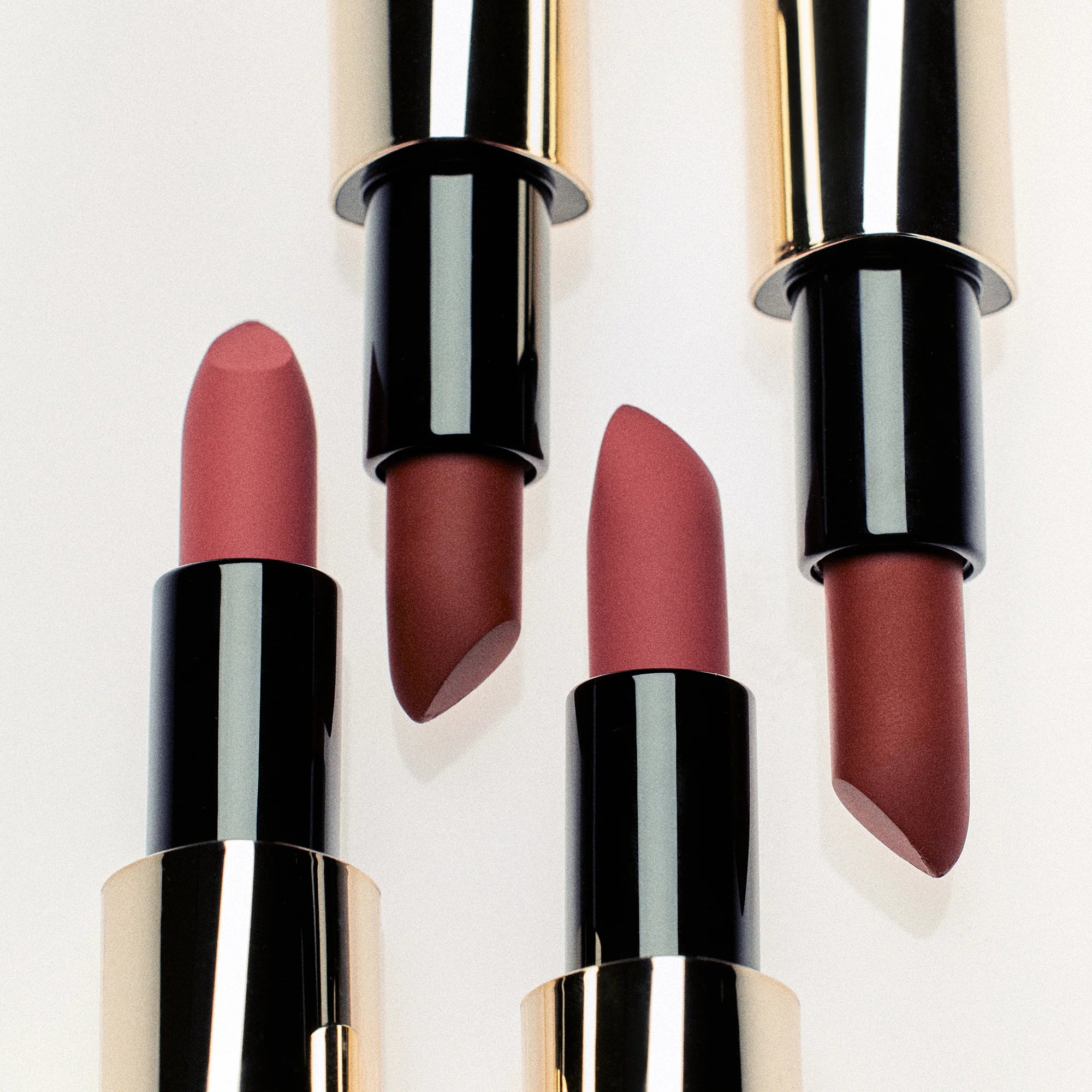 Set of four lipsticks with black and gold cases on a light background