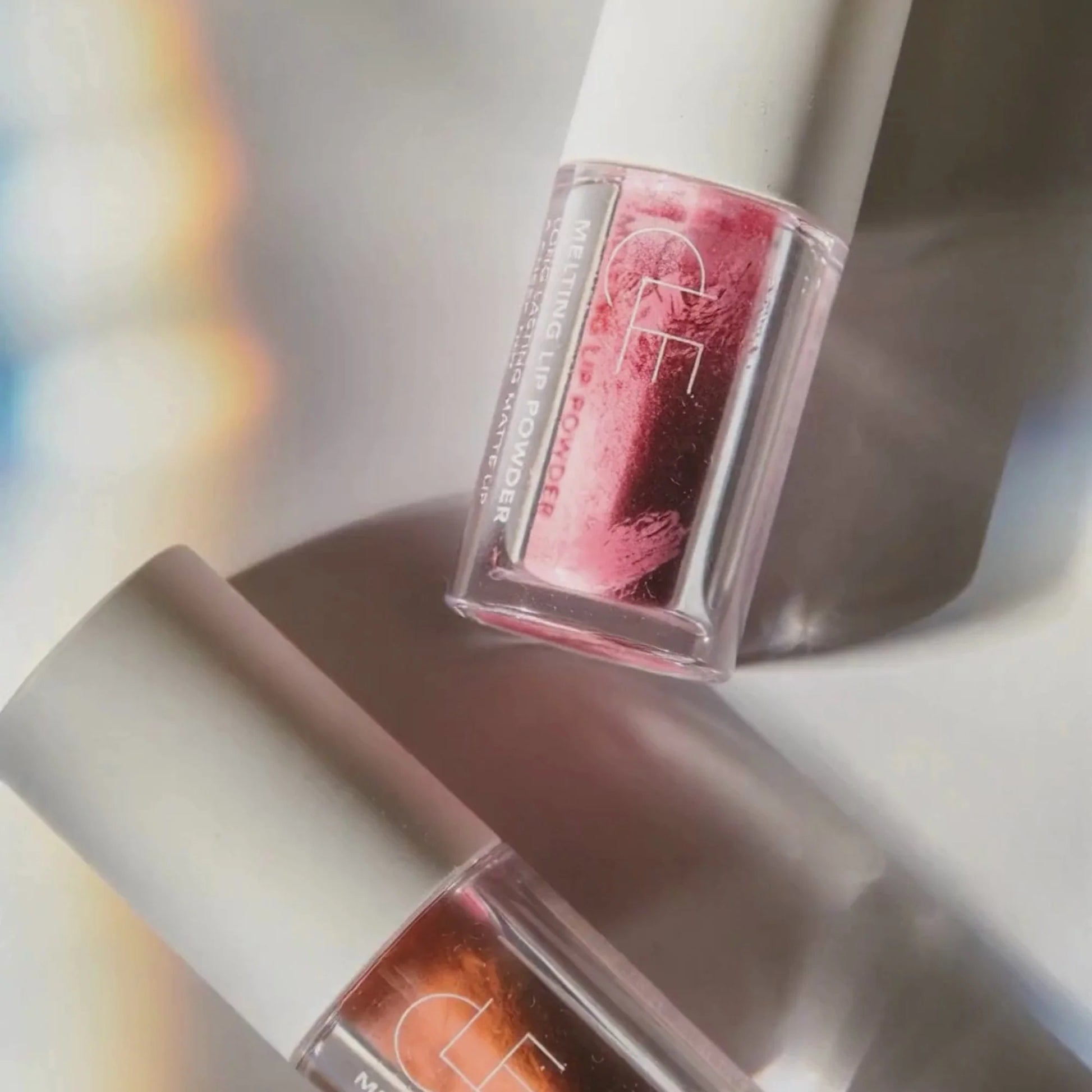 Two lip glosses with a brand logo on a reflective surface