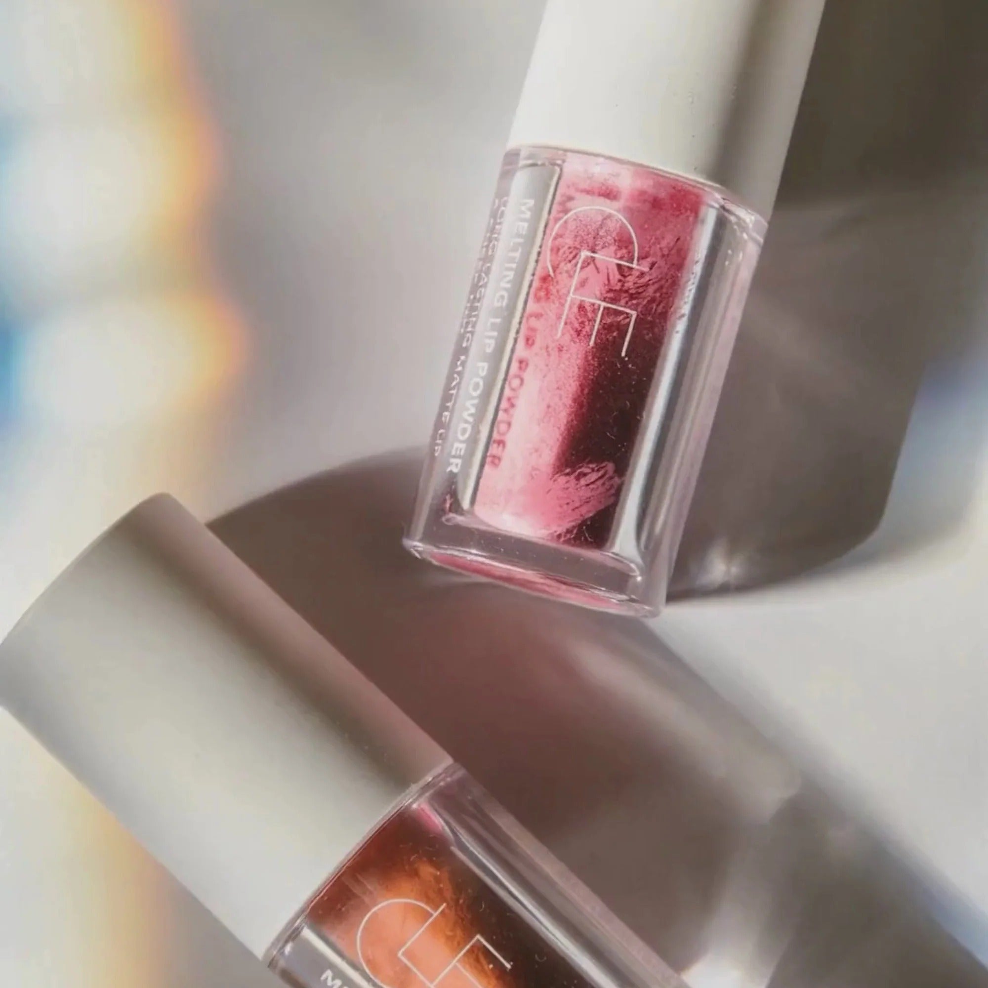 Two lip glosses with a brand logo on a reflective surface