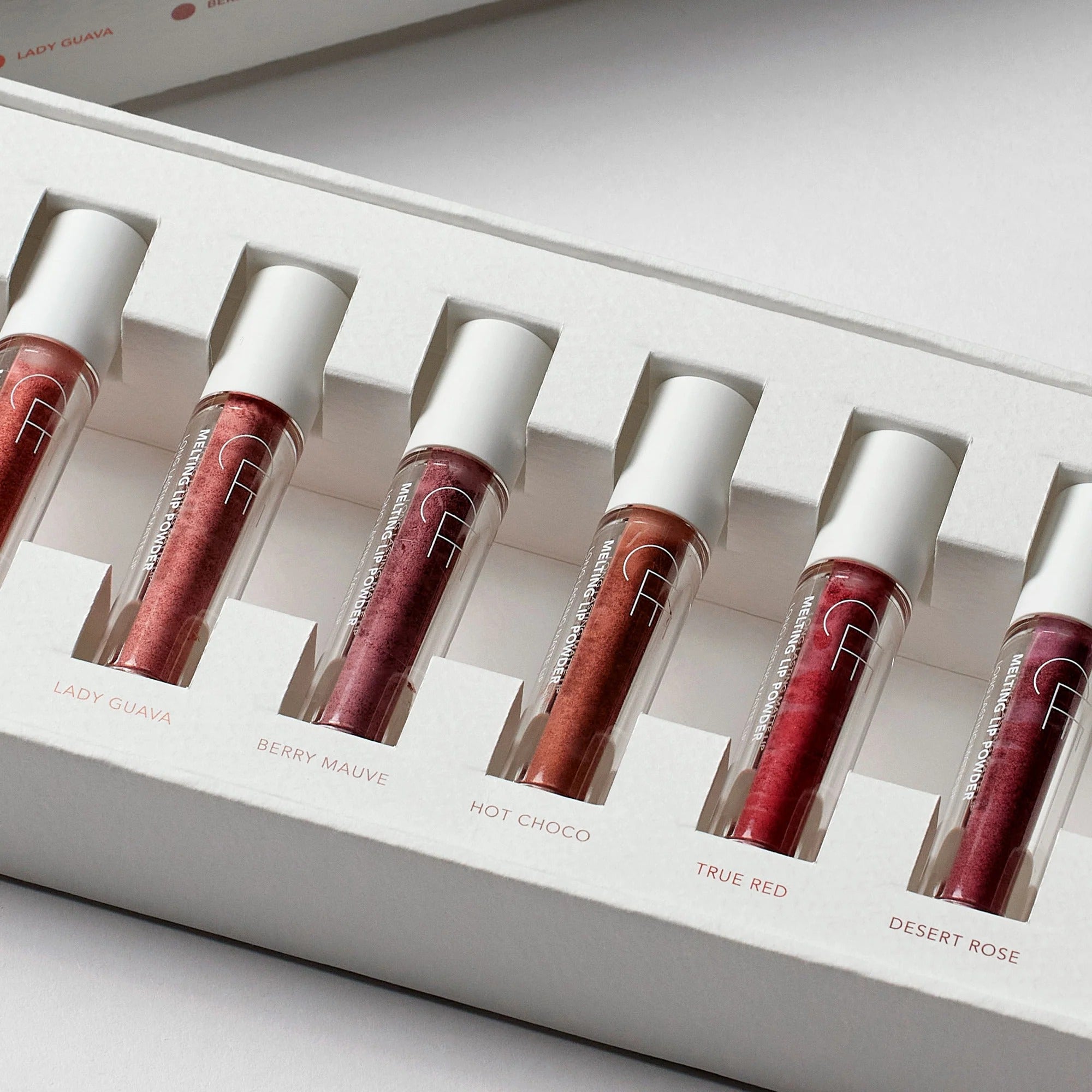 Set of six lip glosses in a white display case with visible brand name.