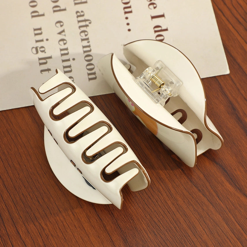 Two white hair clips with gold accents on a wooden surface.