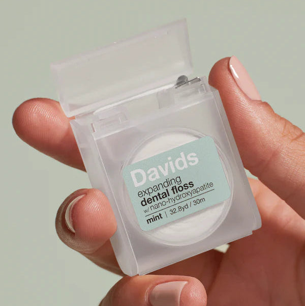 Hand holding a package of Davids expanding dental floss against a light green background