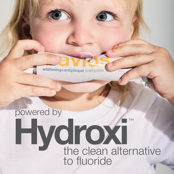 Child holding a tube of Avis toothpaste with 'Hydroxi' branding and text about fluoride replacement.