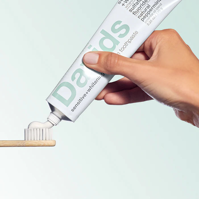 Hand holding a tube of David's toothpaste with a wooden toothbrush.