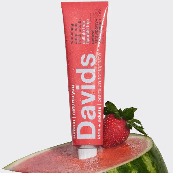 Tube of David's strawberry-flavored protein powder on a watermelon slice with a strawberry.
