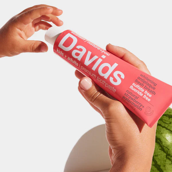 Person holding a pink 'Davids' toothpaste tube with a green apple in the background