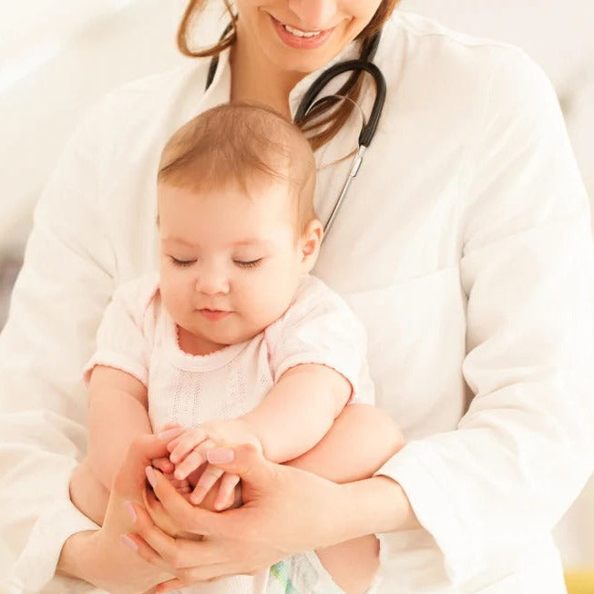 Doctor holding a baby with a stethoscope, surrounded by a soft focus background